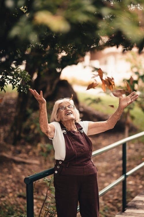 An older participant catching falling autumn leaves in the park.